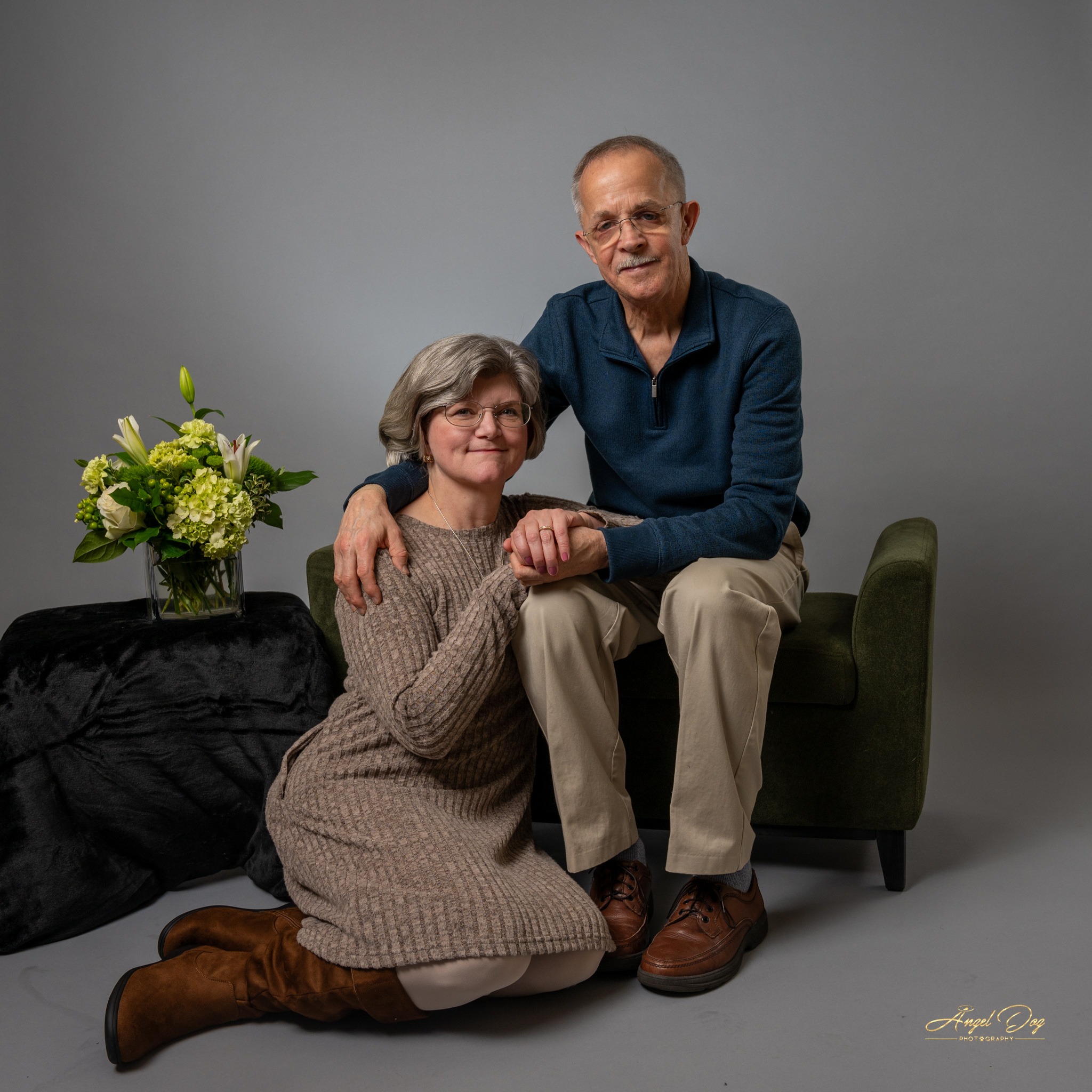 Couple with man in a chair and the woman is sitting on the floor. They are holding hands